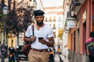 Fototapeta na wymiar Stylish black man walking on the city street using smartphone