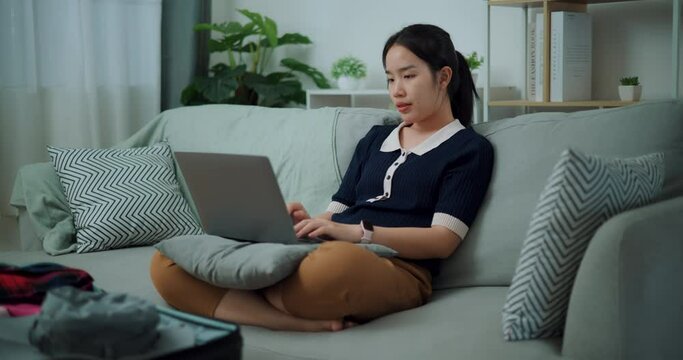 Footage slow motion shot, Asian teenager woman sitting on sofa using laptop for prepare booking hotel and airplane ticket for travel. backpacker travel concept.