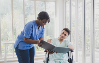 Fototapeta premium Portrait patient caucasian man sit wheelchair with woman nurse carer physical therapist African-American two people talk sign important documents advice feel relax smile happy in hospital room service