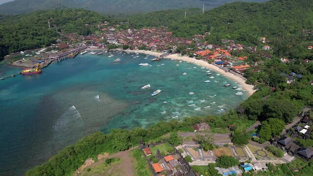 Backward reveal aerial shot of Padangbai Bay and town and Pura Luhur Silayukti hindu temple on sunny day. Manggis, Bali, Indonesia.