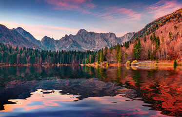 Mangart mountain range reflected in the calm waters of Fusine lake. Amazing summer sunrise in...