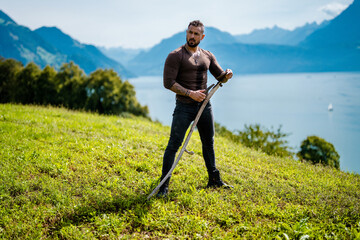 This is a farmer. Man using scythe, cut grass on green farm field. Farmer cut grass. Rural farmer...