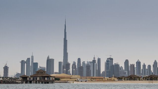 Dubai Downtown skyline with waves on sea beach, United Arab Emirates or UAE. Financial district in travel vacation concept.
