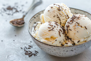 Vanilla Ice Cream with Chocolate Sprinkles. Scoops of rich vanilla ice cream sprinkled with chocolate sprinkles in a speckled ceramic bowl on light background.