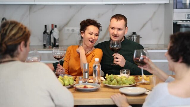 Two married couples are sitting at table, enjoying food and wine, chatting, talking, laughing. In homely atmosphere, friends celebrate anniversary