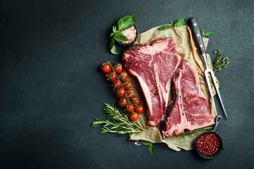 Dry-aged Raw T-bone or porterhouse beef steak with herbs and salt. On a black stone background. Barbecue.