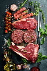 A set of steaks and veal meat. Meat products. On a black stone background. Top view.