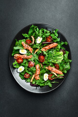 Fresh healthy salad. Salad with arugula, salted salmon, avocado, quail eggs and mushrooms. In a black plate. Diet food.