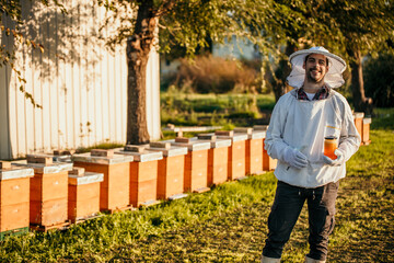 Diligent beekeeper outdoors, holding a jar filled with pure, natural honey