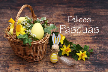 Cesta decorativa de Pascua con narcisos, hiedra y un huevo de Pascua con el texto Felices Pascuas. - obrazy, fototapety, plakaty