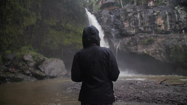Woman in front of waterfall under the rain and in the middle of the jungle. Bali, Indonesia. High quality FullHD slow motion footage.