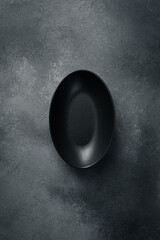 Ceramic oval black plate. Close up on gray concrete background. Free space for text.