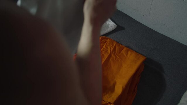 Close up of male prisoner putting orange prison uniform, bath towel and toilet paper on the bed. Inmate takes uniform clothes and gets dressed. Guilty criminal serves term in jail or detention center.