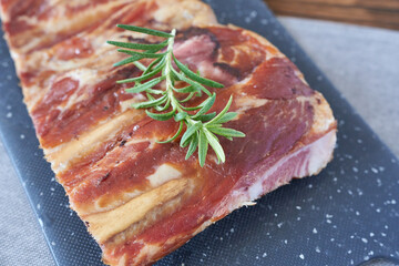 Smoked ribs with rosemary on a black cutting board, close-up.
