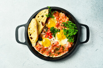 Fried eggs. Shakshuka middle east meal in iron frying pan with toasted bread, pepper, chili, tomato and garlic. Gray concrete table. Top view. Close up