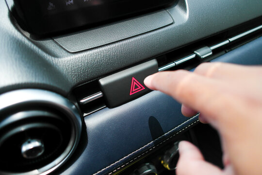 The hazard or emergency light button is pressed by the driver hand. Automotive concept
