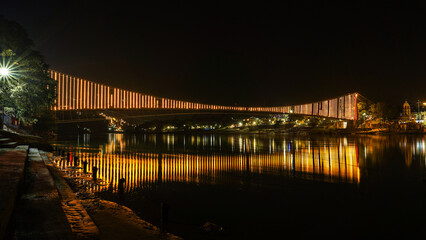 RAMJHULA .Capture the scene from the bridge itself: Gazing down from the bustling Ram Jhula in Rishikesh, the mighty Ganges River flows majestically below, flanked by the colorful city on either side.