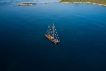 Expensive classic wooden sailing yacht on blue water morning sun top view. Classic modern wooden sailing yacht anchored off the coastline of the island of Sardinia, top view.