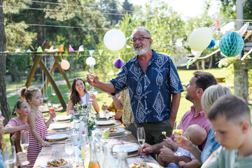 Grandfather holding champagne glass. Senior man making celebratory toast at outdoor summer garden...