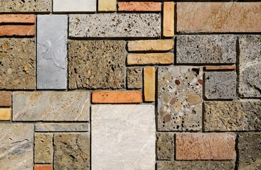 Multicolored external wall made of different types of rocks and bricks arranged geometrically. Background and texture.