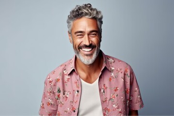 Handsome middle aged man laughing and looking at camera while standing against grey background