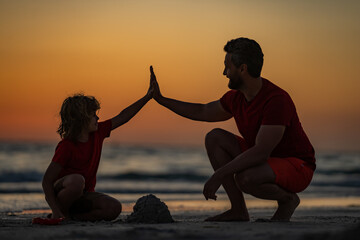 Kid and father building sandcastle. Father and son playing on the beach. Father and child son on tropical beach on sunset. Sand castle. Father with son on the sea. Fathers giving Five hand.