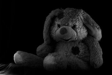 Sitting stuffed bunny. Image depicting a touching stuffed rabbit seated, on a black background. His...