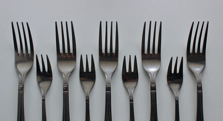 Top parts of identical dessert and table forks laid out in even rows 
