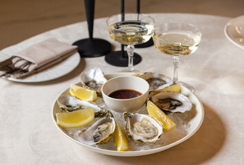 Fototapeta premium open oysters on plate with slice of lemon on ice cubes on table.candles in the chandelier in restaurant, woman hand taking dressing with spoon putting in sea fruit.romantic dinner
