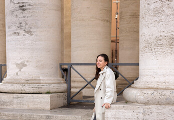 giant white columns and road between.woman female posing, in long coat. girl sitting in sunlight and shadow dropped on asphalt. architectural antic temple.