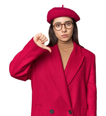 Stylish young Caucasian woman in red trench coat and beret on studio background showing a dislike gesture, thumbs down. Disagreement concept.