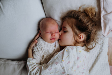 Portrait of big sister cuddling newborn, little baby. Girl lying with her new sibling in bed,...