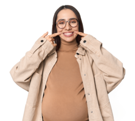 Pregnant young Caucasian woman showcasing maternity on studio background smiles, pointing fingers at mouth.
