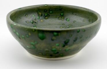 A green and white ceramic bowl sits atop a wooden table. The bowl is empty and shows a simple, elegant design.