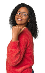 African American woman in studio setting points with thumb finger away, laughing and carefree.