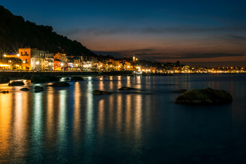 Fototapeta premium night town coast with flashlights from embarkment and reflection in sea gulf water with golden urbal lights and blue hour sky on background of landscape