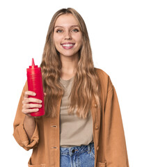Blonde woman holding ketchup bottle in studio setting happy, smiling and cheerful.