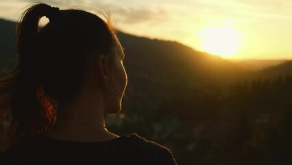 Young woman enjoying sunset in mountains alone. Female hiker portrait looking at scenic landscape of valley at foot of the mountains, rear view