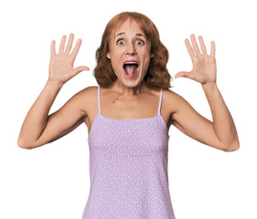 Redhead mid-aged Caucasian woman in studio receiving a pleasant surprise, excited and raising hands.