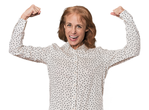 Redhead mid-aged Caucasian woman in studio showing strength gesture with arms, symbol of feminine power
