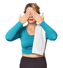 Caucasian woman in sportswear with towel afraid covering eyes with hands.