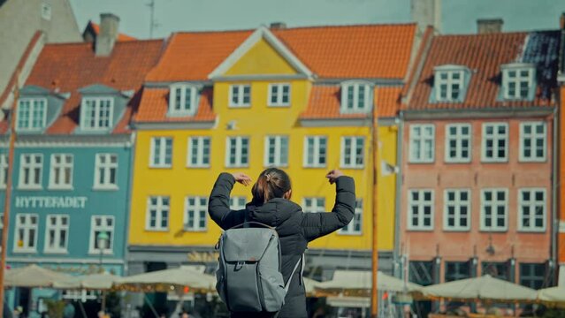 Happy Asian tourist woman backpacker traveler enjoying at Copenhagen Nyhavn, Famous landmark, northern Europe destination, the old town waterfront water canal in the capital Kobenhavn in Denmark.