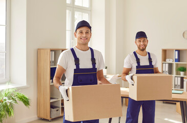 Portrait captures the teamwork of two men, professional movers, carrying cardboard boxes during an...