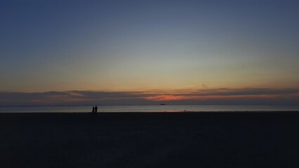 People silhouette are experiencing pure joy as they gather on the beach, delighting in the mesmerizing sunset.