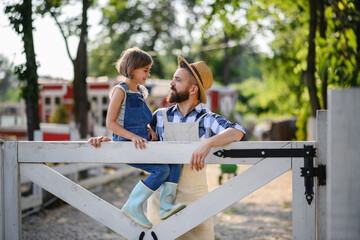 Farmer family, father with daughter sitting on wooden fence on family farm. Concept of...