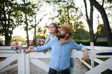 Fototapeta premium Portrait of farmer family, father and young daughter standing on wooden fence on family farm. Concept of multigenerational farming.