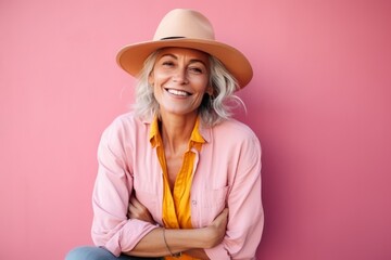 Portrait of a happy senior woman with hat over pink background.