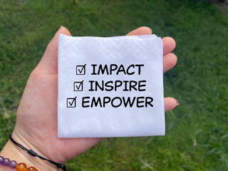 Motivational and inspirational wording. IMPACT, INSPIRE, EMPOWER written on a tissue. Blurred styled background.