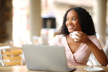 Black woman thinking and drinking with a laptop - obrazy, fototapety, plakaty