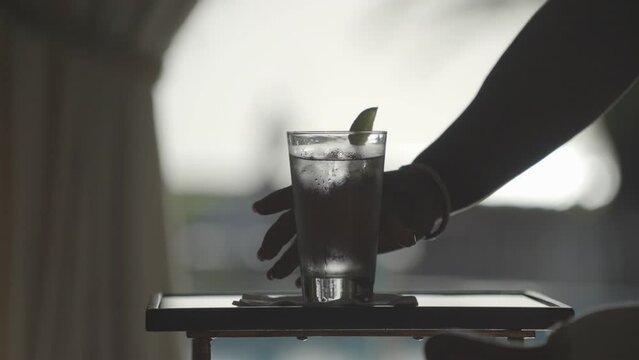 Beverage being set on wooden table by waiter, water, gin tonic or vodka soda with ice cubes and lime. Close up.